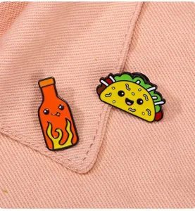 Close up view of cute cartoon hot sauce and taco enamel pins, showing vibrant colors and details.