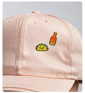 Close-up detail view of cute taco and hot sauce enamel pins decorated on a soft pink cap.