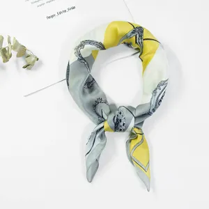 Detalle de pañuelo cuadrado de seda con estampado geométrico y nudo en azul y amarillo.