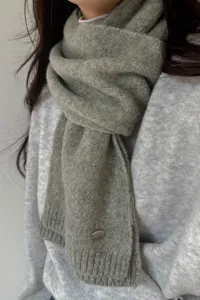 Nahaufnahme des weichen grünen Strickschals mit Metallschild, gemütlich und warm.