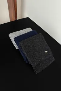 Detailaufnahme gestapelter Strickschals für den Winter mit weicher Textur und Metall-Etikett.