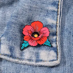 Close-up detail of retro color-blocking red flower enamel pin brooch on denim fabric background.