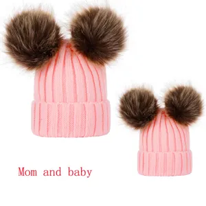Mom and baby matching pink knitted beanies with fluffy double pom poms for winter warmth.