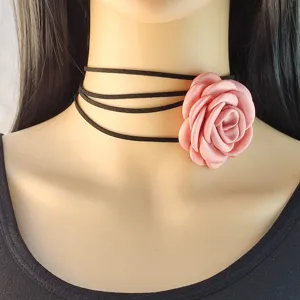 Primo piano di una collana girocollo vintage con cordino nero e fiore di camelia rosa.
