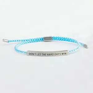 Vista dettagliata del bracciale in corda intrecciata azzurro con barra in acciaio incisa.