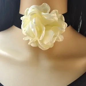 Primo piano dettaglio di un fiore di camelia in tessuto bianco vintage su collana girocollo nera.