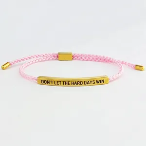 Dettaglio bracciale intrecciato rosa fatto a mano con tubo in metallo dorato inciso.