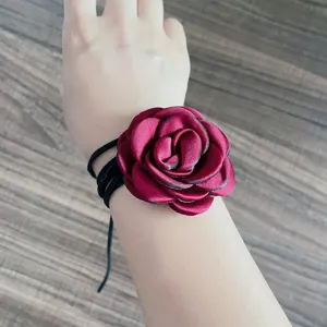 Dettaglio di un girocollo o bracciale con fiore di rosa in tessuto rosso e lacci neri.
