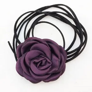 Vista dettagliata della rosa in tessuto viola scuro con cordoncini in pelle scamosciata nera.