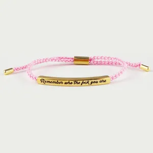 Bracciale in corda intrecciata rosa con barra incisa dorata e citazione motivazionale.