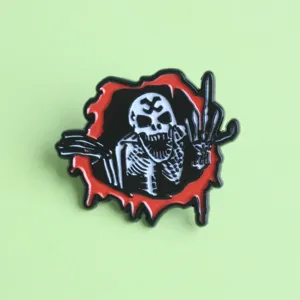Gros plan de détail du pin's émaillé squelette horreur punk avec un design de griffe en métal.