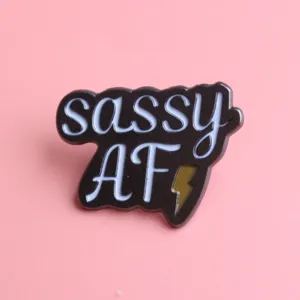 Detail shot of black and white metal enamel pin featuring sassy letters and lightning bolt.