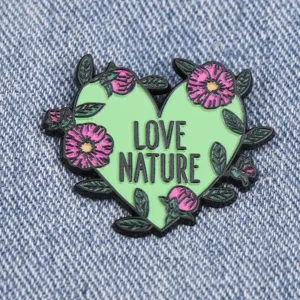 Gros plan d'un pin's emaille coeur vert avec des fleurs roses et le texte love nature detail.