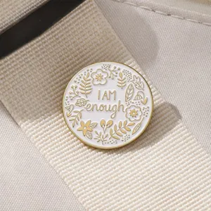 Nahaufnahme der goldgeränderten Emaillebrosche mit Blumenkranz und inspirierendem Text.
