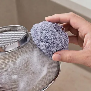Hand hält einen lila Nano-Faser-Reinigungsball, um ein Edelstahlsieb zu schrubben