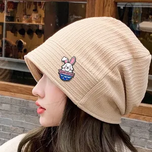 Beige knit slouchy hat featuring a cute Easter bunny alloy brooch pin accessory detail shot.