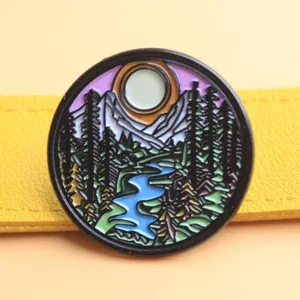 Round landscape enamel pin badge featuring mountains, trees and river design for bags.