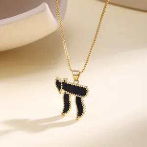 Detail view of a gold chain necklace with a black enamel Hebrew Chai pendant and beaded edges.