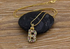 Close-up detail of gold-plated colorful zircon letter B pendant necklace on black stone.