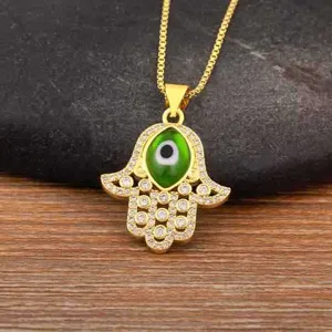 Detailed close-up of a gold-plated Hamsa hand necklace with a green evil eye and sparkling zircon stones.