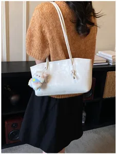 Detail view of a white PU leather shoulder tote bag with cute plush pendant for daily commute.