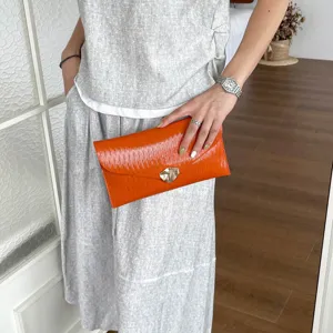 Detail view of orange gloss clutch bag featuring envelope flap and unique metallic clasp design.