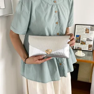 Silver metallic envelope clutch bag featuring a unique golden dog clasp fashion detail.