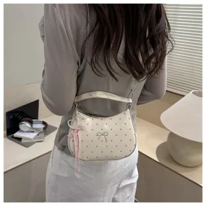 Detail shot of a cream crescent shoulder bag featuring pink polka dots, bow and charm.