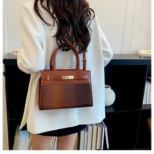 Detail view of brown crocodile texture top handle shoulder bag with metal turn-lock.