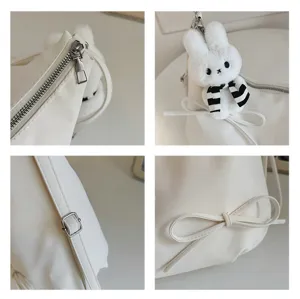 White shoulder bag detail view showcasing plush bunny charm, zipper and elegant bow knot.