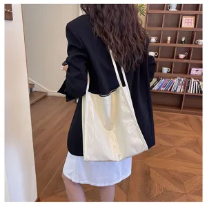 Detail view of a glossy white shoulder tote bag showcased in a modern indoor setting.