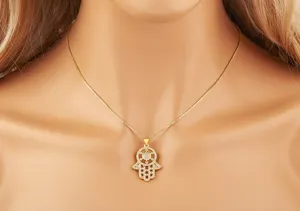 Close-up detail of a gold-tone hamsa hand pendant necklace with sparkling clear zircon stones.