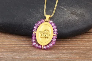 Primo piano del ciondolo ovale placcato oro 18K con ali d'angelo e perline rosa sfaccettate.