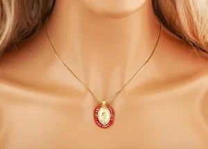 Gedetailleerde close-up weergave van de 18k vergulde ovale Maagd Maria hanger ketting met rode kralen.