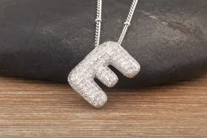 Close up of a sparkling cubic zirconia iced out letter E pendant necklace on a pebble.