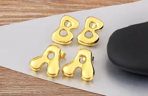 Close-up of trendy gold bubble letter stud earrings, showing glossy metallic finish details.