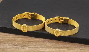 Gold plated mesh letter bracelet detail view showing alphabet charms G and O on dark slate.