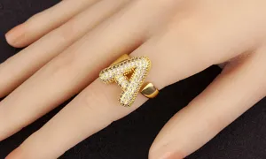 Nahaufnahme des klobigen goldenen Buchstaben-A-Rings mit funkelnden Zirkoniasteinen am Finger.