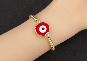 Gros plan sur le bracelet œil maléfique rouge plaqué or avec détail de perles au poignet