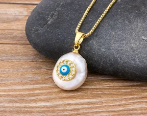 Detailed close-up of a gold box chain necklace featuring a baroque pearl and evil eye pendant.