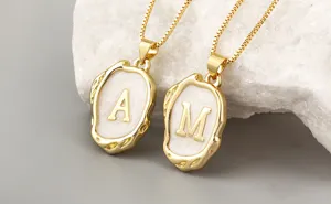 Gold plated letter pendant necklace detail featuring stylish irregular geometric shapes and white enamel.