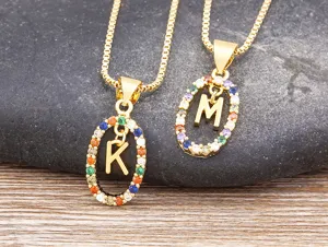 Close-up of gold-plated colorful cubic zirconia letter pendant necklaces on natural stone detail.