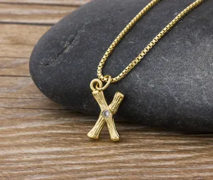 Close-up detail of the 18k gold plated letter X necklace with bamboo texture and crystal.