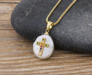 Detailed close-up of a gold-plated cross pendant featuring multicolored zircon stones on a baroque pearl.