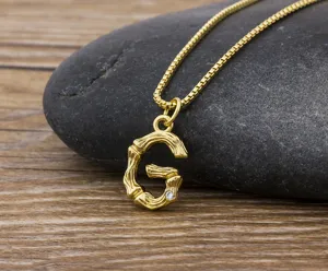 Detail view of 18k gold plated bamboo letter G necklace pendant on dark stone background.