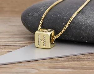 Close-up detail of gold-plated cubic zirconia letter H cube pendant necklace on stone.