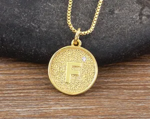 Close-up detail of gold letter F pendant necklace with sparkling stone accent on textured coin.