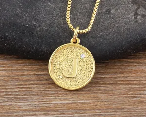 Detail view of a minimalist 18k gold plated brass zircon letter J round pendant necklace.