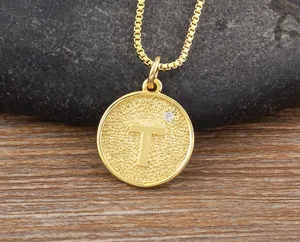 Close-up detail of gold letter T pendant necklace with sparkling zircon on stone background.