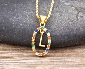 Close-up of gold letter L pendant necklace with colorful zirconia stones on stone background.